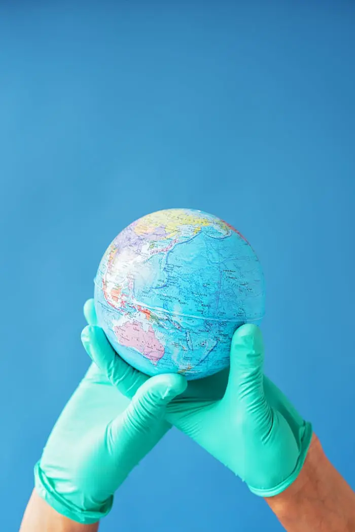 Hands in latex gloves holding a globe against a bright blue background, symbolizing global care.